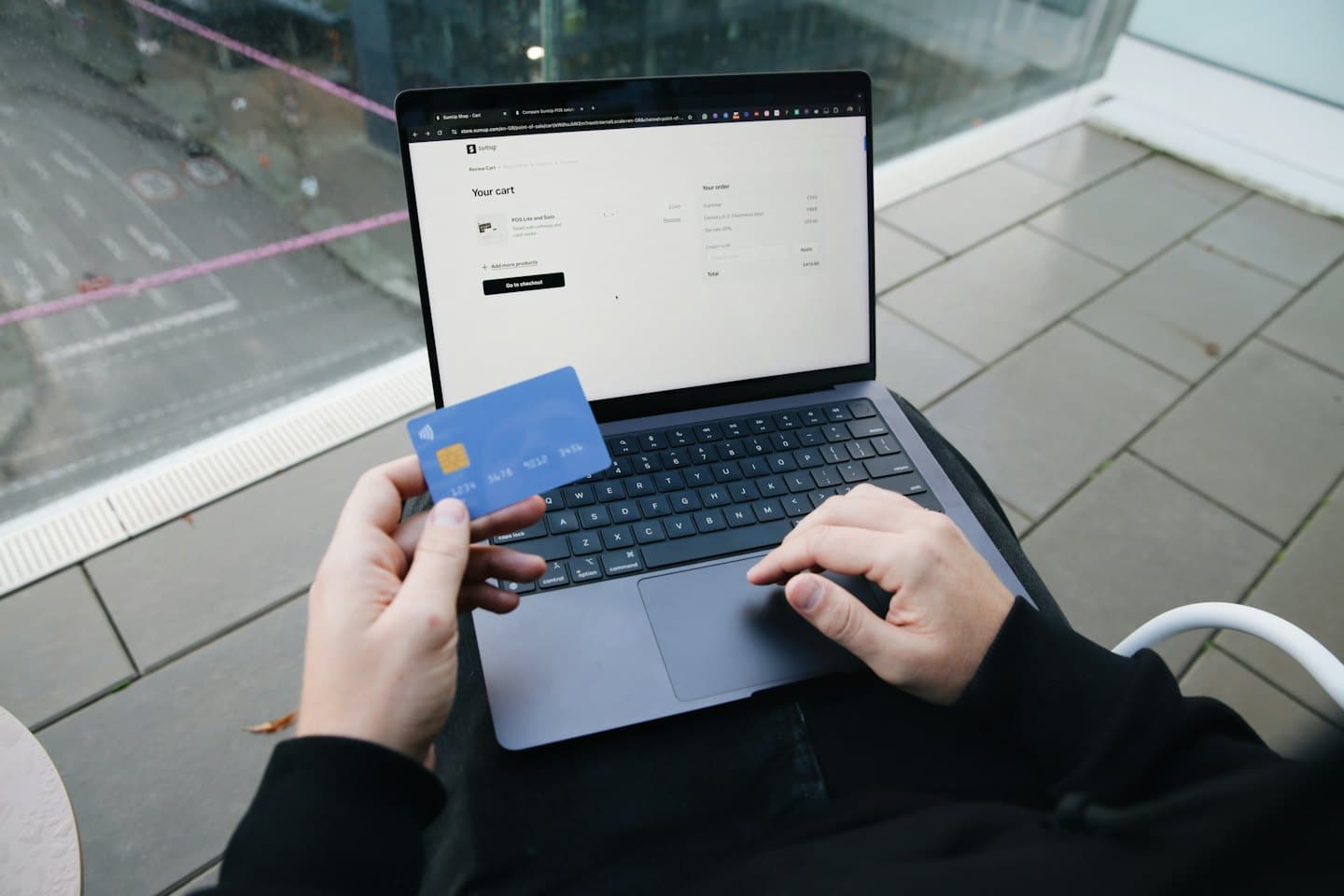 Dłonie trzymające niebieską kartę kredytową nad koszykiem na zakupy na laptopie.